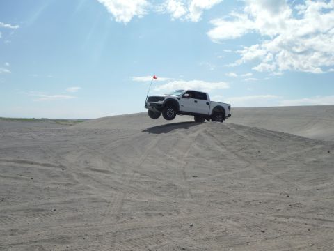 2005 Jeep Wrangler - Pickup truck catches air while driving over a sand dune on a sunny day.