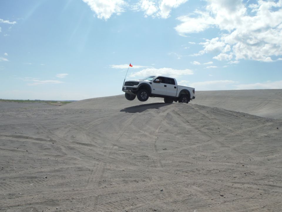 White pickup truck airborne over a sand dune with a red flag attached