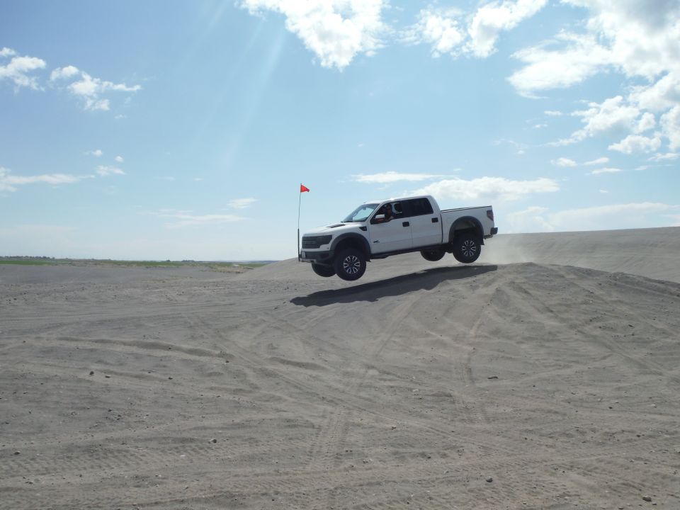 White pickup truck airborne over a sand dune, red flag visible on a pole