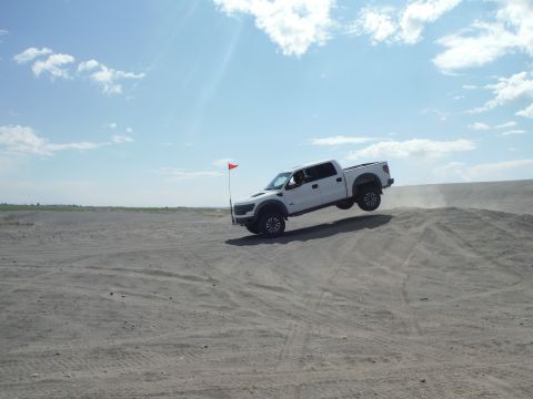2005 Jeep Wrangler - A white Ford F-150 Raptor navigates sand dunes with its front wheels lifted off the ground.