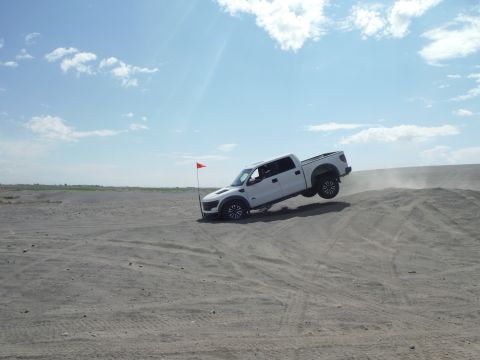 2005 Jeep Wrangler - Pickup truck airborne while cresting a sand dune under a partly cloudy sky.