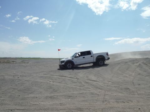 2005 Jeep Wrangler - A white pickup truck navigates sandy terrain, kicking up dust under a bright, cloudy sky.