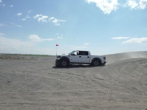 2005 Jeep Wrangler - A white pickup truck drives on a sandy dune under a partly cloudy sky.