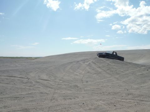 2005 Jeep Wrangler - A black pickup truck navigates a sandy incline on a clear day, with tire tracks visible in the sand.