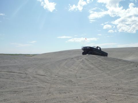 2005 Jeep Wrangler - A dark off-road vehicle navigates a sandy terrain under a partly cloudy sky.