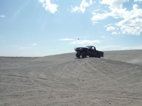 2005 Jeep Wrangler - A black pickup truck navigates a sandy terrain under a partly cloudy sky.