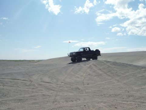2005 Jeep Wrangler - A black pickup truck navigates a sandy terrain on a bright, cloudy day.