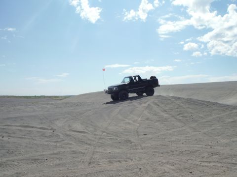 2005 Jeep Wrangler - A black pickup truck drives on a sand dune on a clear day.