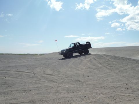 2005 Jeep Wrangler - A black pickup truck navigates a sandy incline under a partly cloudy sky.
