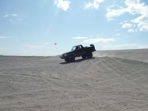 2005 Jeep Wrangler - Pickup truck navigates a sandy terrain on a bright, clear day.