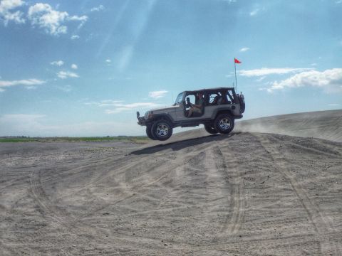 2005 Jeep Wrangler - A 2005 Jeep Wrangler navigates a sandy terrain, kicking up dust as it crests a dune.