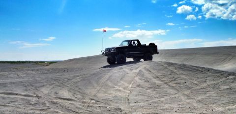 2005 Jeep Wrangler - A black pickup truck navigates a sandy terrain, kicking up dust under a bright blue sky.
