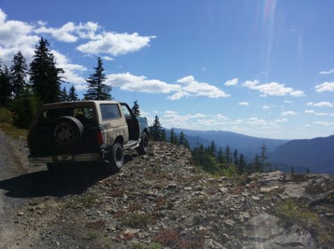 1996 Ford Bronco - Two SUVs parked on a rocky mountain overlook with a scenic view of distant mountains and clouds.