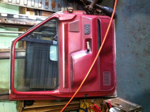 1988 Ford Bronco - A red truck door, detached from the vehicle, is visible in a workshop setting.