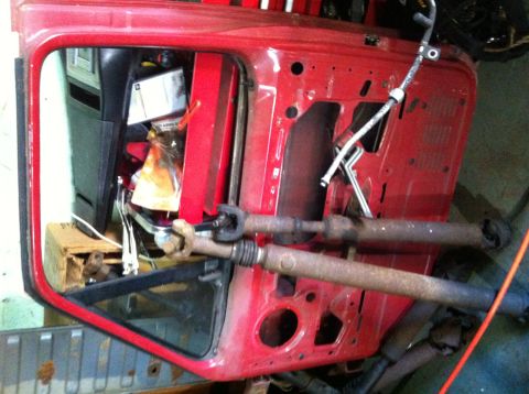 1988 Ford Bronco - A red vehicle door is shown with two driveshafts in the foreground, suggesting it is a part for a larger vehicle.