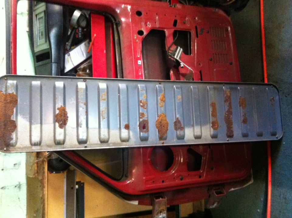 Rusted tailgate panel resting on red vehicle body, showing interior components