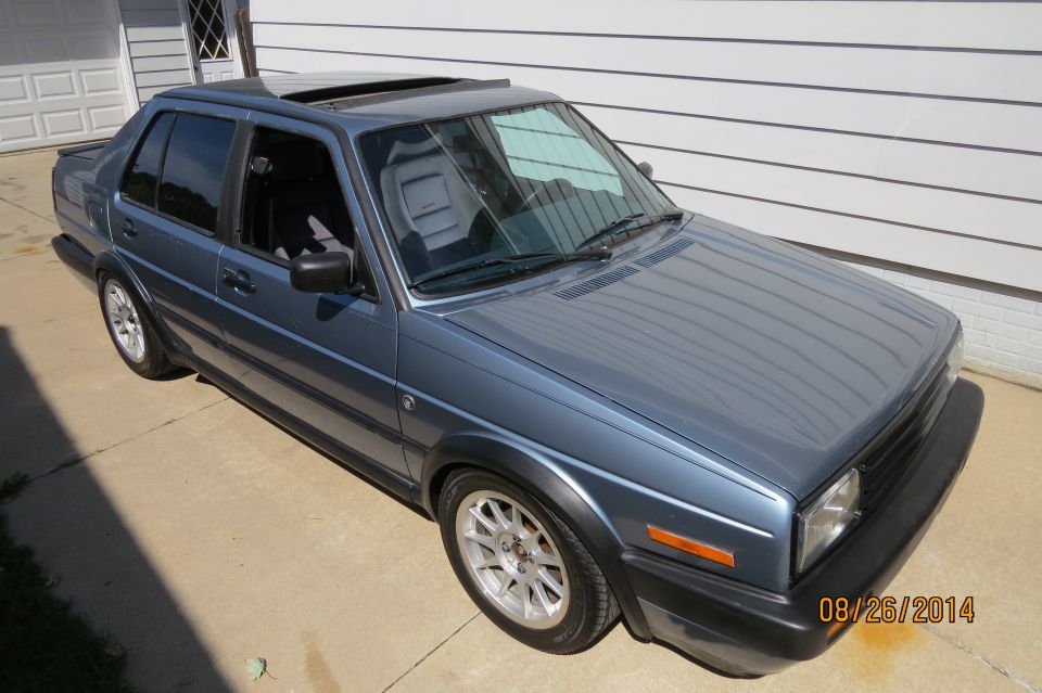 1990 Volkswagen Jetta sedan, blue, with sunroof and aftermarket wheels, parked in front of a garage