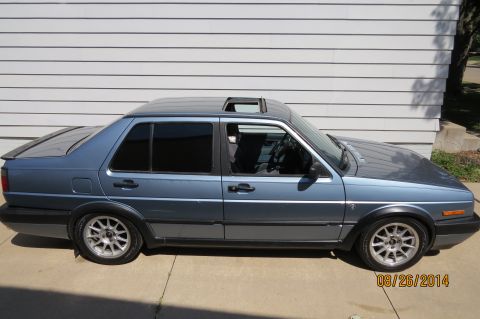 1990 Volkswagen Jetta - A blue 1990 Volkswagen Jetta is parked outside a building with a white paneled wall.