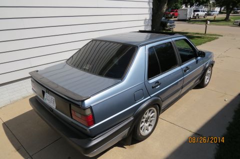 1990 Volkswagen Jetta - A blue 1990 Volkswagen Jetta is seen from a three-quarter front angle, parked next to a house.