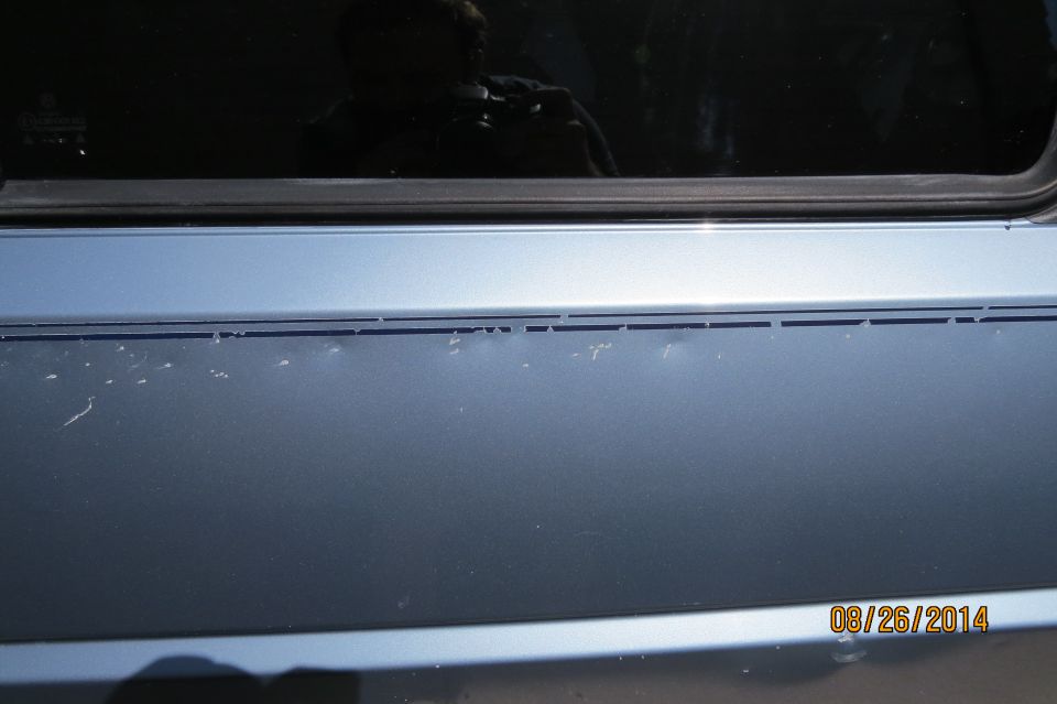 Blue car door with minor paint chips and a reflection of a person holding a camera in the window