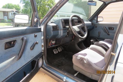1990 Volkswagen Jetta - The interior of a 1990 Volkswagen Jetta features blue fabric seats and door panels, a dark dashboard, and a four-spoke steering wheel.