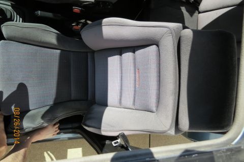 1990 Volkswagen Jetta - Interior view of car seats, showing fabric upholstery and a small red logo on the passenger seat. A foot is visible near the open door.