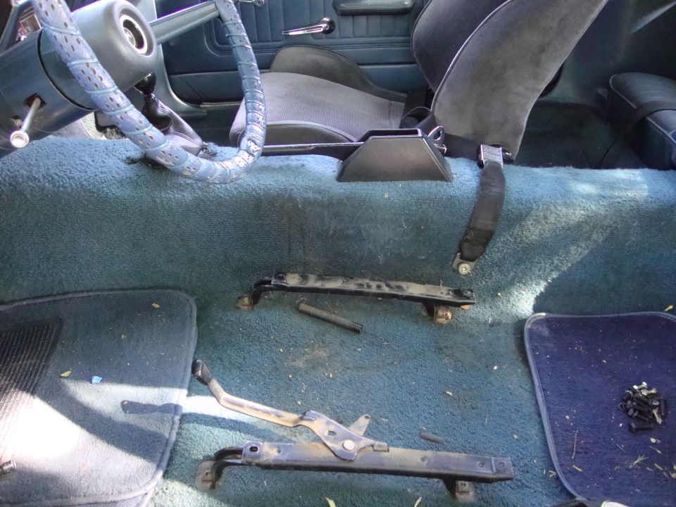 Car interior with blue carpet and seats, showing removed seat rails and steering wheel