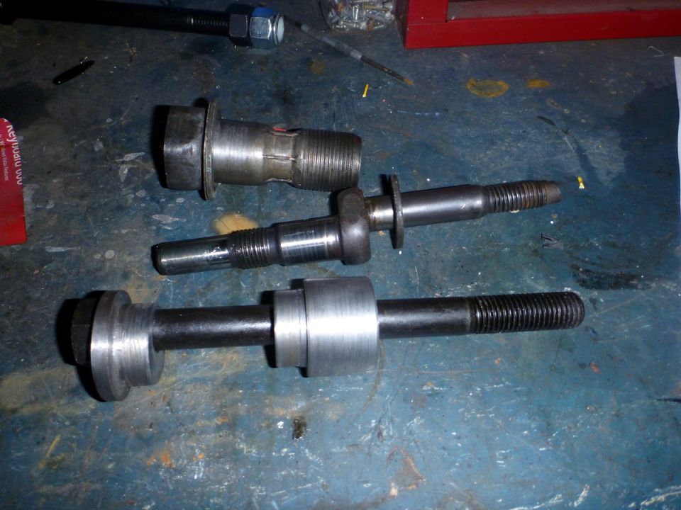 Three metal suspension components on a blue workbench