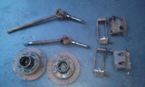 1994 Ford Bronco - Front brake parts, including rotors, calipers, and spindles, are laid out on a blue surface.