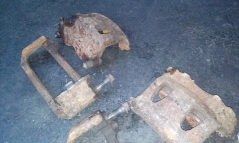 1994 Ford Bronco - Two heavily rusted brake calipers and a C-clamp tool are displayed on a dark, textured surface.