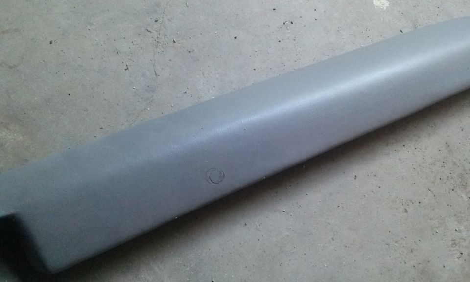 Gray plastic trim piece with a circular indentation, lying on a concrete surface