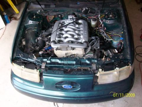 1993 Ford Taurus - The engine bay of a 1993 Ford Taurus is open, revealing the V6 engine and its complex wiring system.