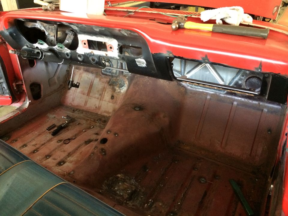 Car interior with dashboard removed, showing bare metal floor and bodywork. Tools are visible on the floor and dashboard