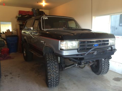 1989 Ford Bronco - Modified Ford Bronco with off-road tires and a custom front bumper sits in a garage.