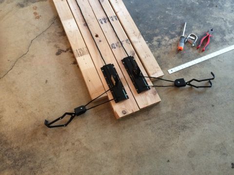 1989 Ford Bronco - Assembly components for a bicycle rack are arranged on wooden planks, alongside a screwdriver, pliers, and a ruler.
