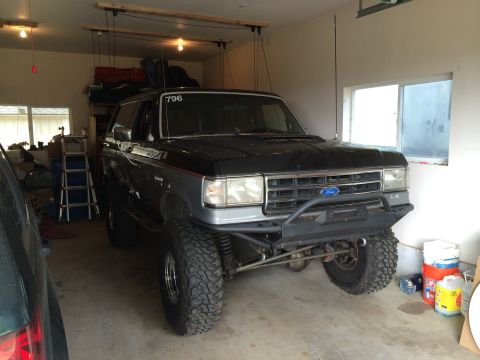 1989 Ford Bronco - Modified 1989 Ford Bronco with off-road tires and custom bumper sits in a garage.