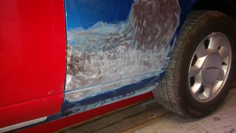 1994 Ford Thunderbird - A car door shows extensive body filler and primer in preparation for accident repairs, with a silver wheel visible.