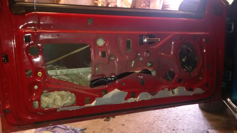1994 Ford Thunderbird - The interior of a red car door is exposed, revealing its inner workings and sound dampening material.