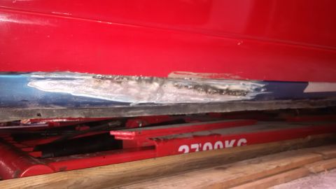 1994 Ford Thunderbird - Close-up of body repair work on a vehicle's lower panel, showing filler and rust damage.