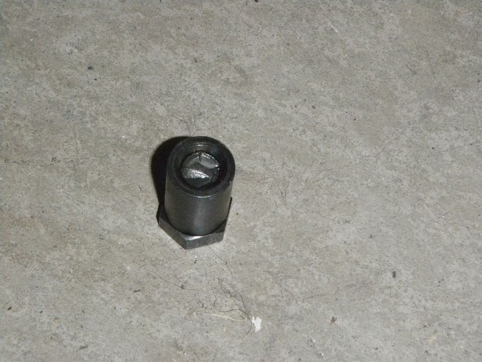 Hexagonal metal part with a cylindrical top, resting on a concrete surface