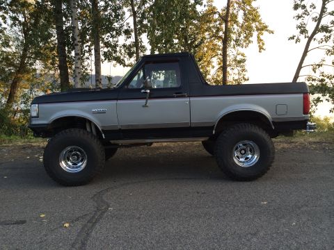 1989 Ford Bronco - Side profile of a lifted 1989 Ford Bronco parked on asphalt with trees in the background.