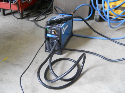 1992 Ford Bronco - A Miller welding machine is connected to cables and hoses, resting on a concrete floor in a workshop.