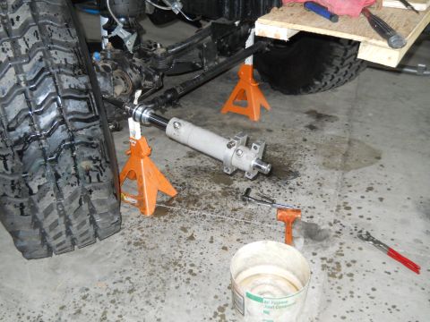 1992 Ford Bronco - Close-up of vehicle suspension and steering parts, including a large tire and a removed steering stabilizer cylinder.