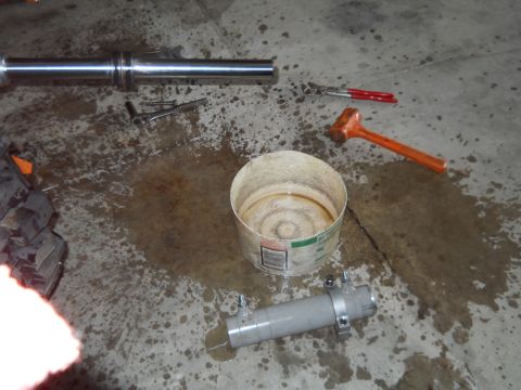 1992 Ford Bronco - Parts of a shock absorber, along with tools and a bucket, are laid out on a wet concrete floor.