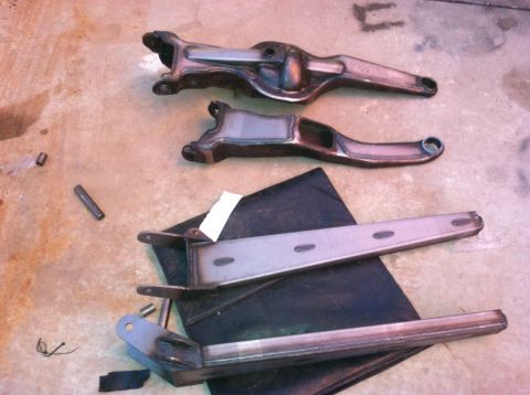 1995 Ford Bronco - Several metal suspension parts are laid out on a concrete surface, with a black mat underneath some of them.