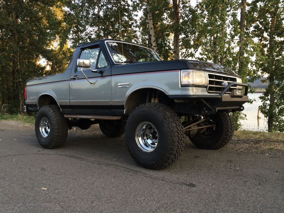 Lifted two-tone gray and black 1989 Ford Bronco with chrome wheels and off-road tires