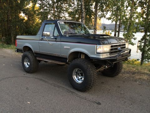 1989 Ford Bronco - Modified 1989 Ford Bronco parked outdoors near water and trees.