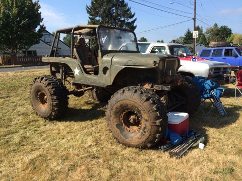 1989 Ford Bronco - A heavily modified off-road vehicle with oversized tires sits on a grassy field, with other vehicles visible in the background.