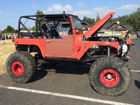 1989 Ford Bronco - A modified red off-road vehicle is parked at an outdoor event with its hood open.