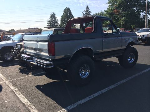 1989 Ford Bronco - A lifted 1989 Ford Bronco with a two-tone gray and black paint scheme and a removable top is parked at an outdoor event.